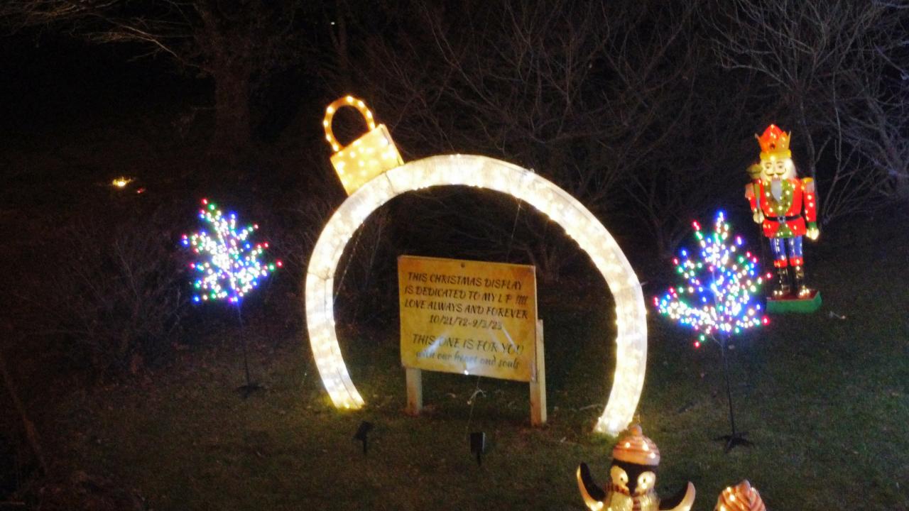 A glowing ornament arch framing the display’s dedication sign, with a nutcracker and lit trees